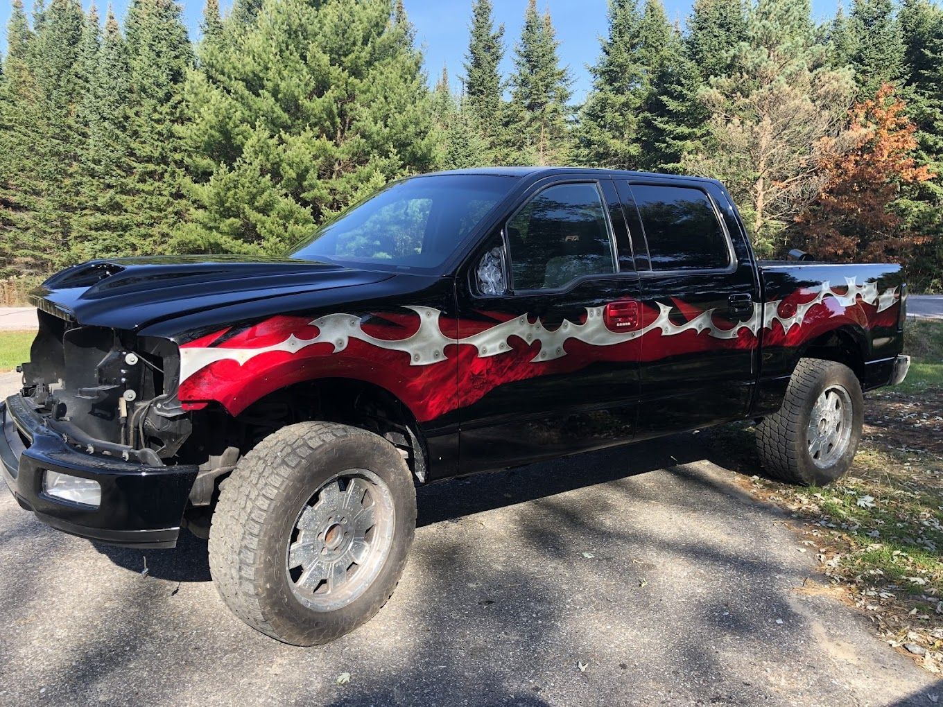 A black truck with flames painted on the side is parked on the side of the road.