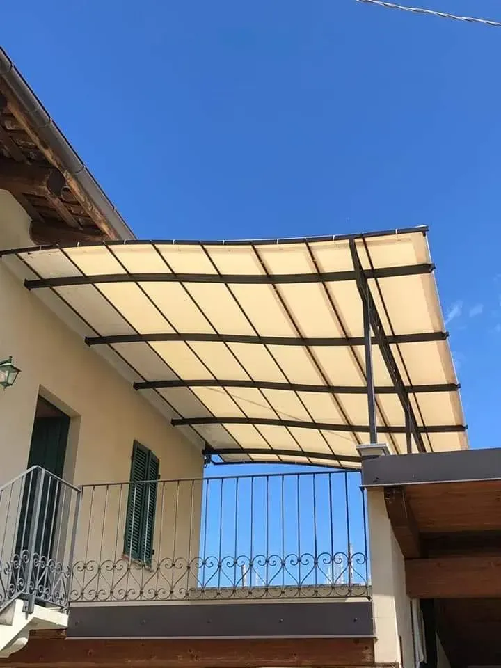 Baldacchino beige su un balcone con struttura in metallo nero, sullo sfondo di un cielo azzurro terso.