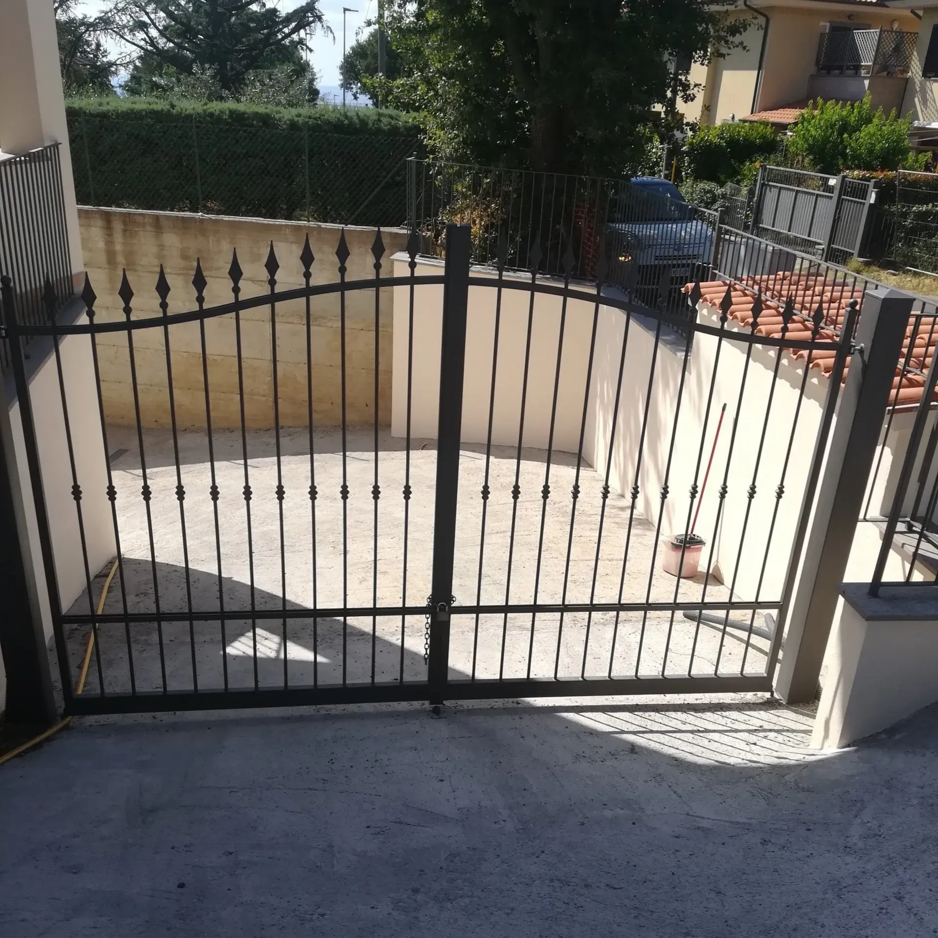 Un cancello in ferro battuto nero davanti a un vialetto in cemento. Sullo sfondo, pareti beige e un'auto.