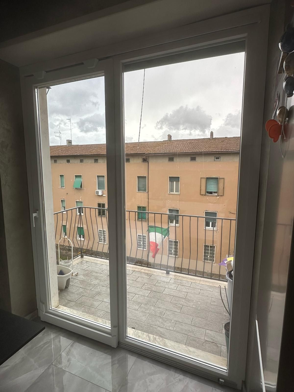 Una vista dall'interno attraverso una porta scorrevole in vetro su un balcone che si affaccia su un condominio.