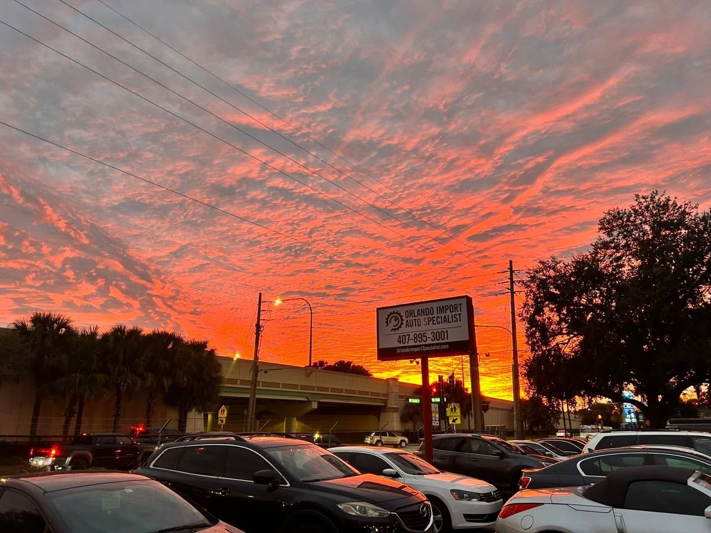 Cars parked in a lot under a vivid orange and red sunset sky. A sign is visible.