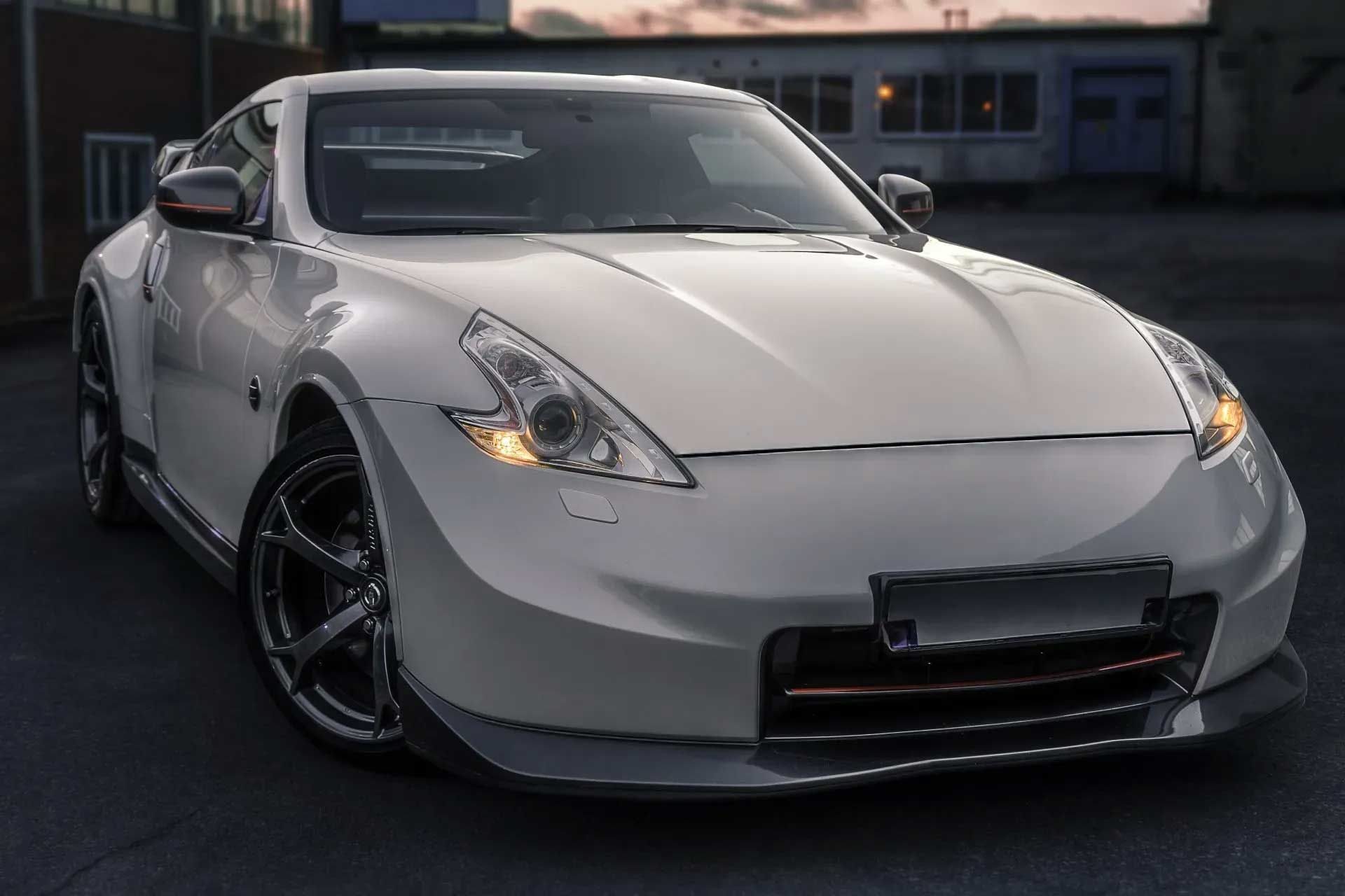 White Nissan 370Z sports car with modifications, parked outdoors in twilight.