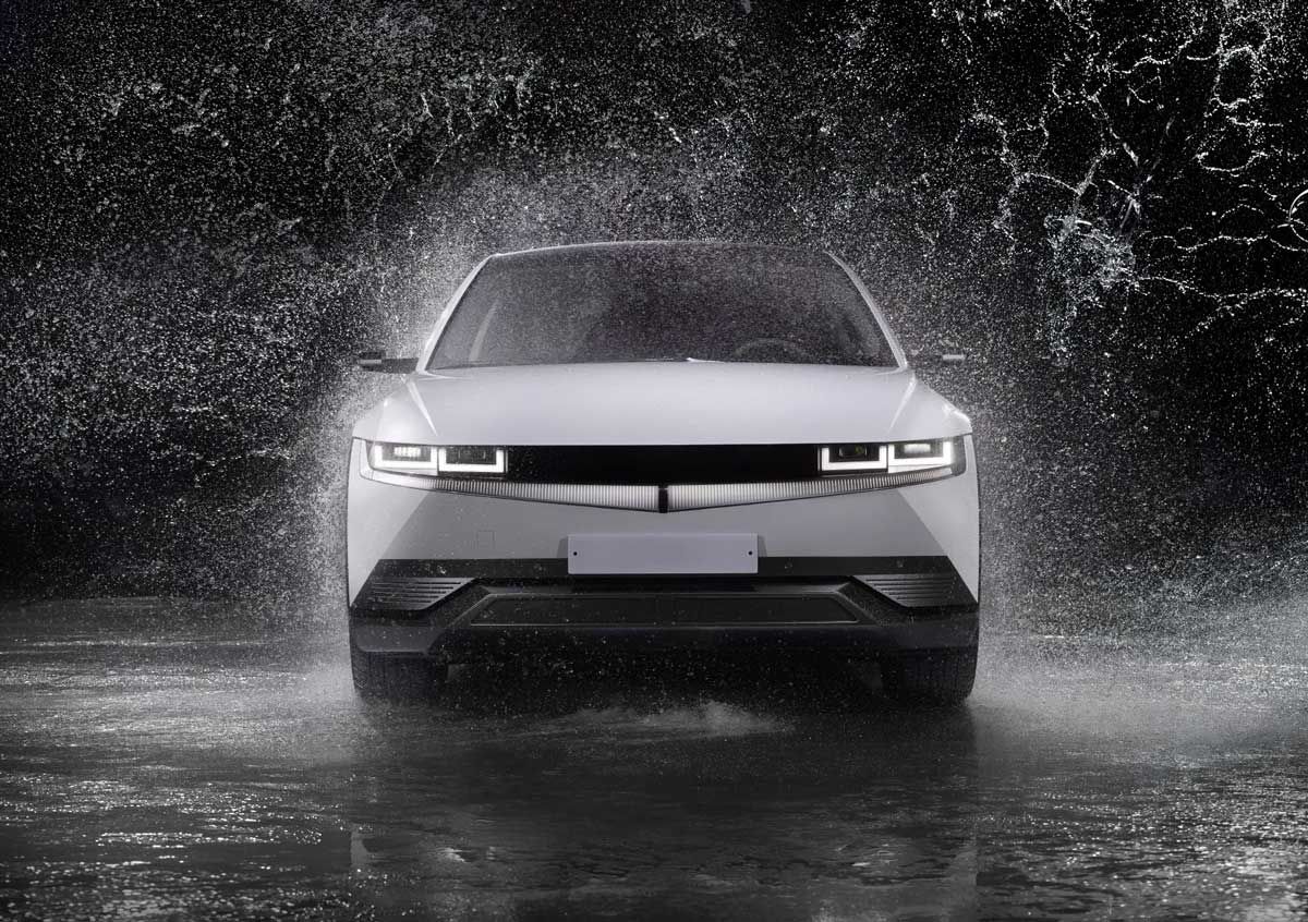 White car driving through water, creating splashes, night setting.