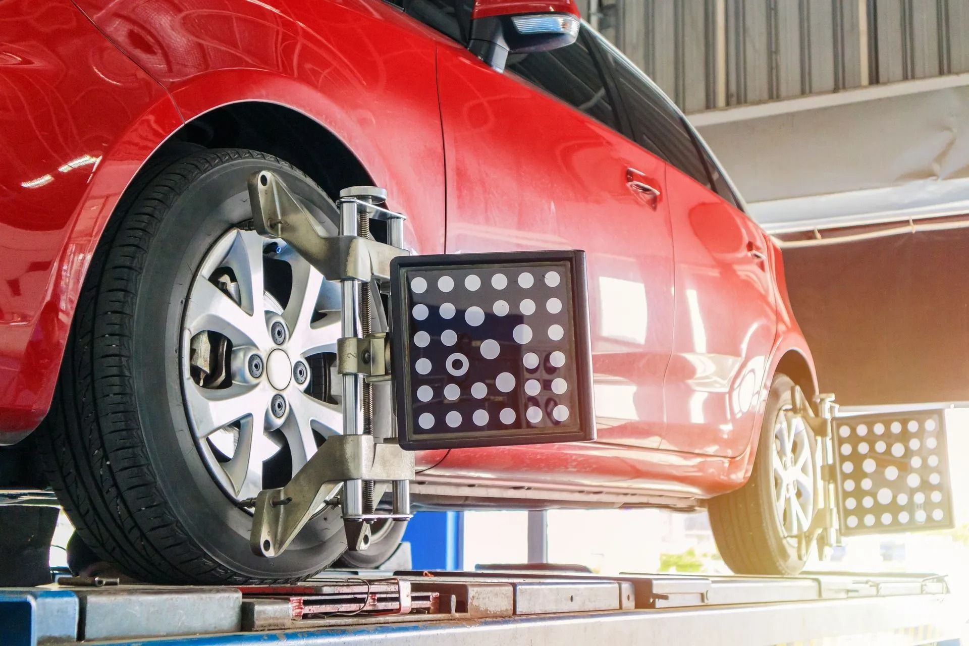 Red car undergoing wheel alignment at a repair shop, with black and white alignment equipment attached to front tire.