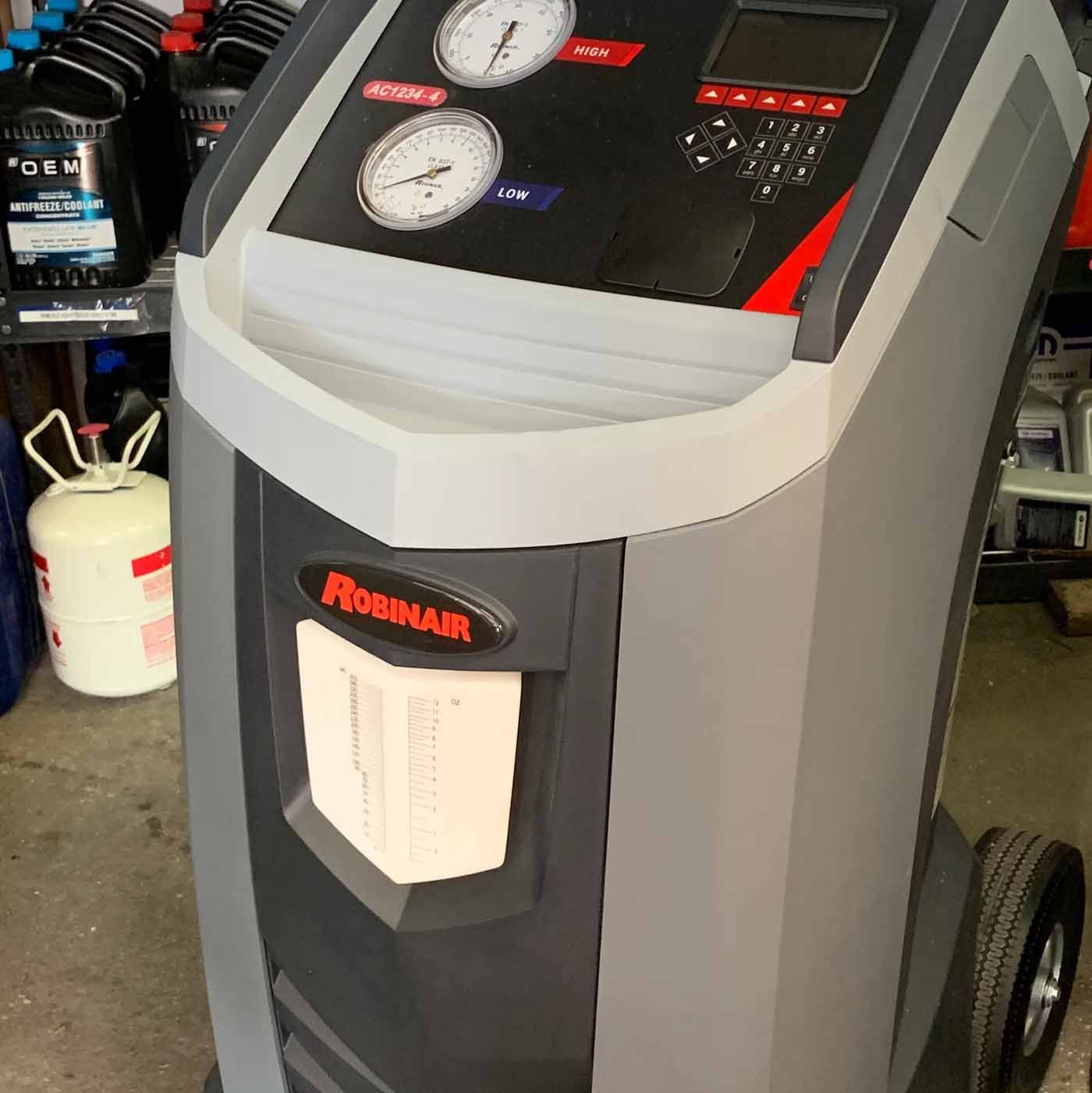 A gray and black automotive air conditioning service machine. It has gauges, a display screen, and the brand name