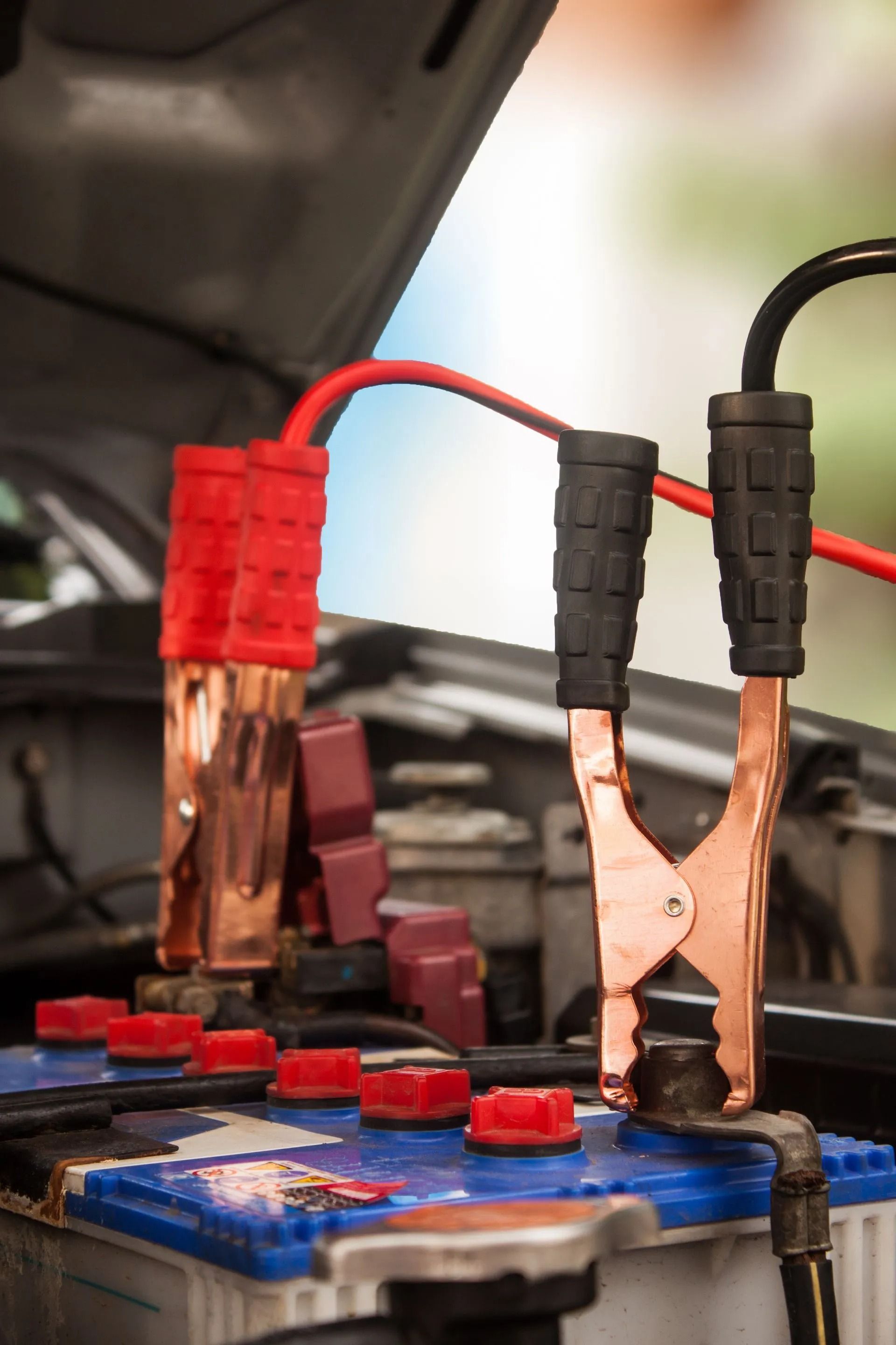 Jumper cables connected to a car battery, red cable on positive terminal, black cable on negative terminal.