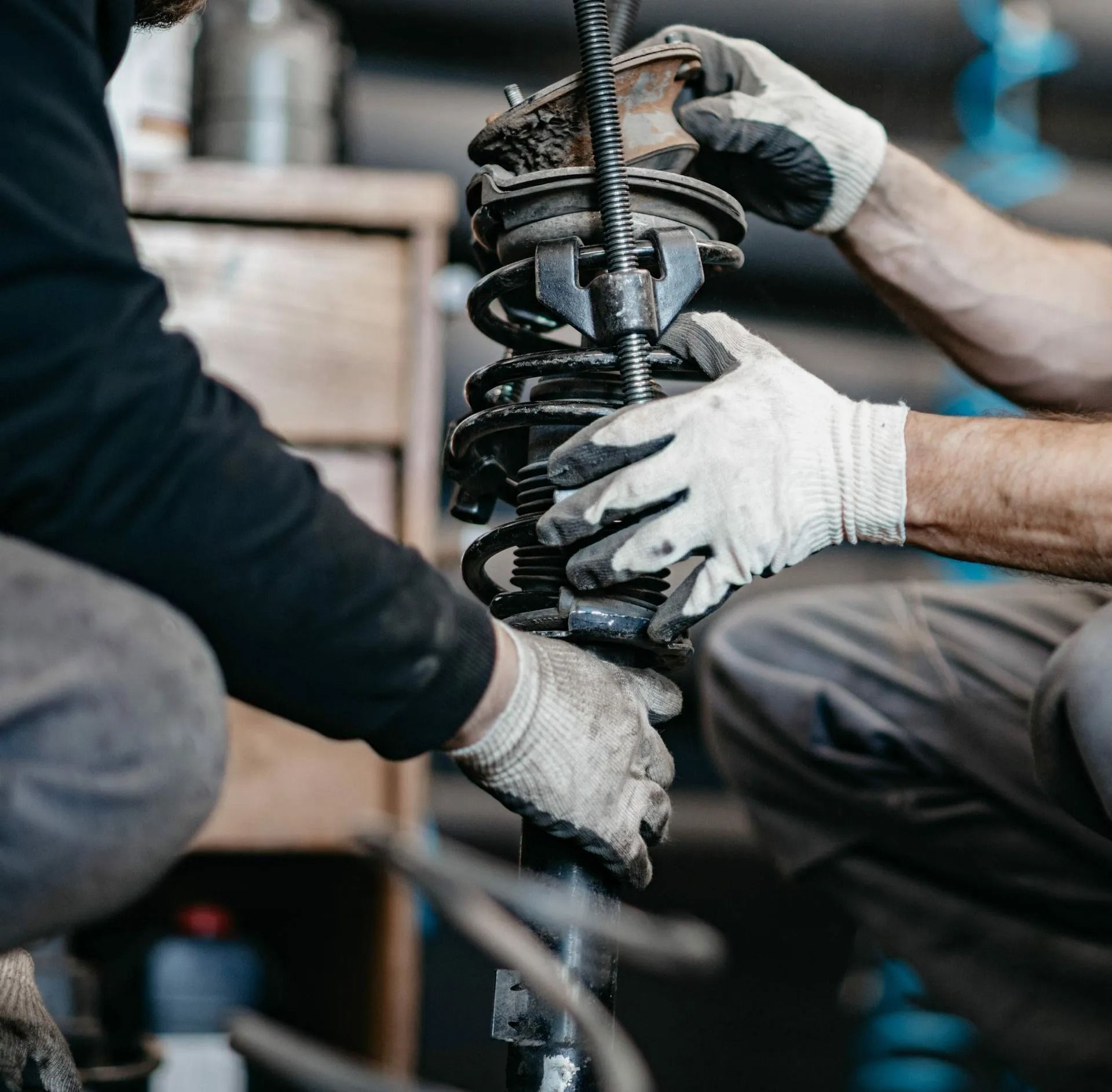 Two mechanics wearing gloves assemble a car shock absorber in a workshop.