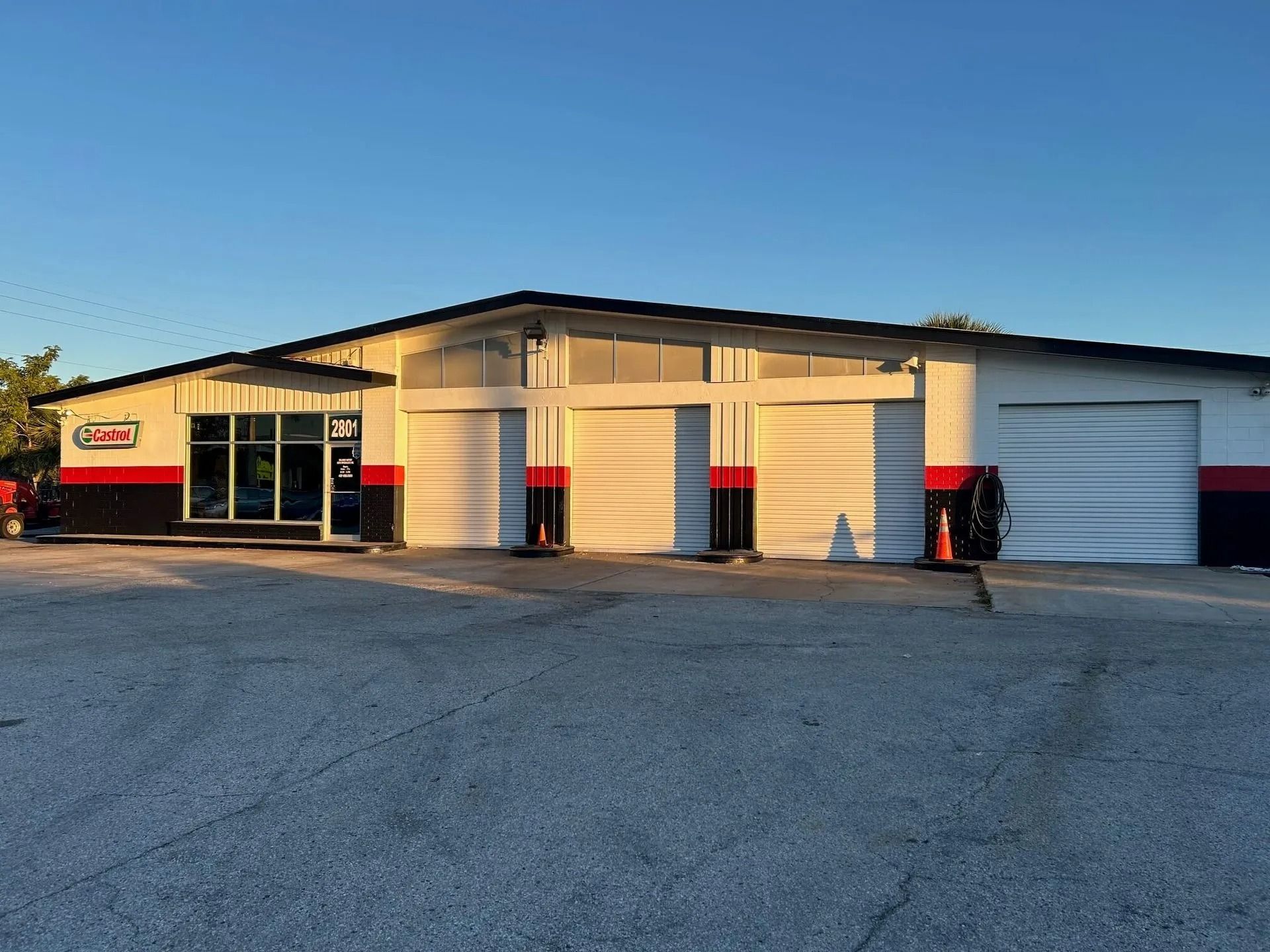 A commercial building, the exterior is white with black and red accents, large garage doors, and a glass entrance.