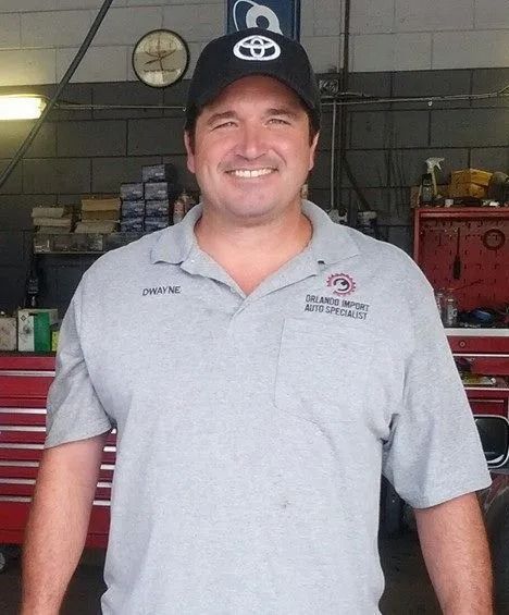 Man in gray polo and Toyota cap smiles in a garage.