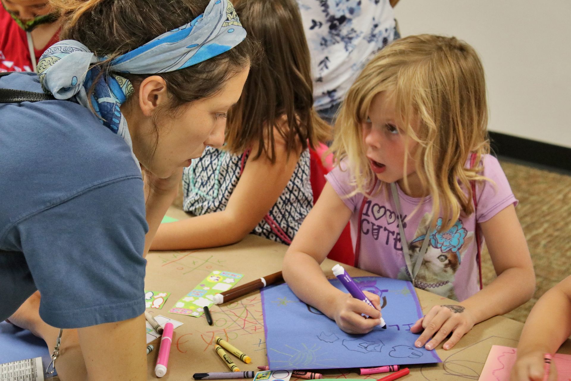 A woman is helping a little girl draw on a piece of paper.
