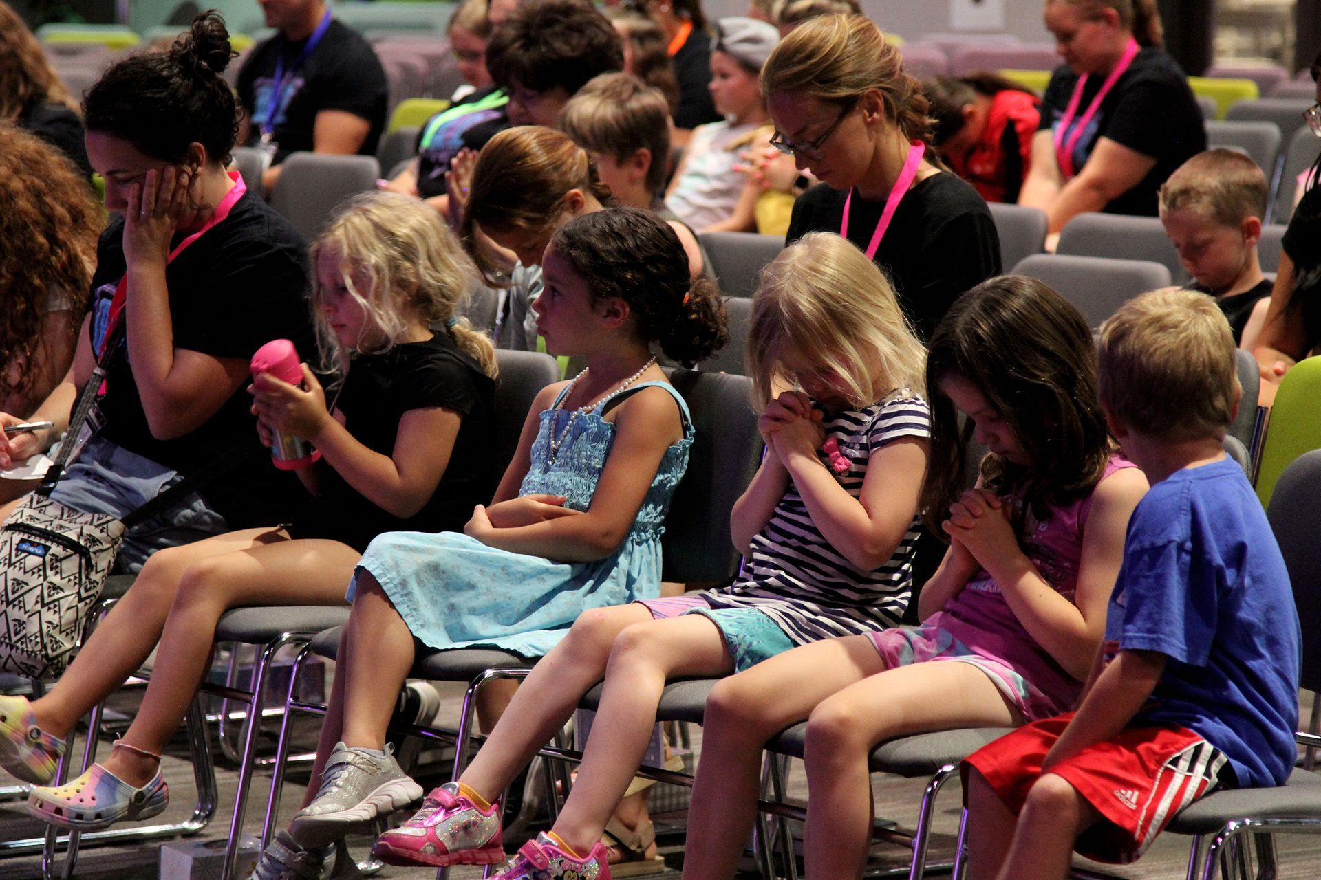 A group of children are sitting in chairs with their hands on their chests.