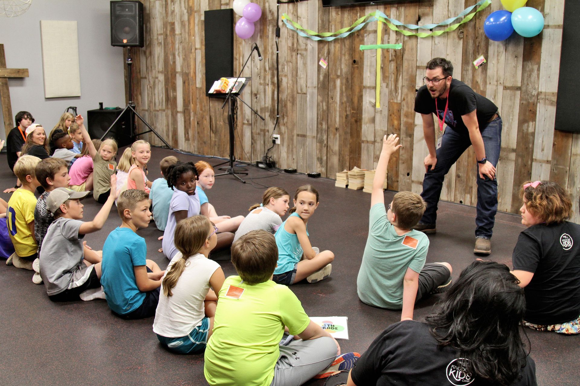 A man is standing in front of a group of children sitting on the floor.