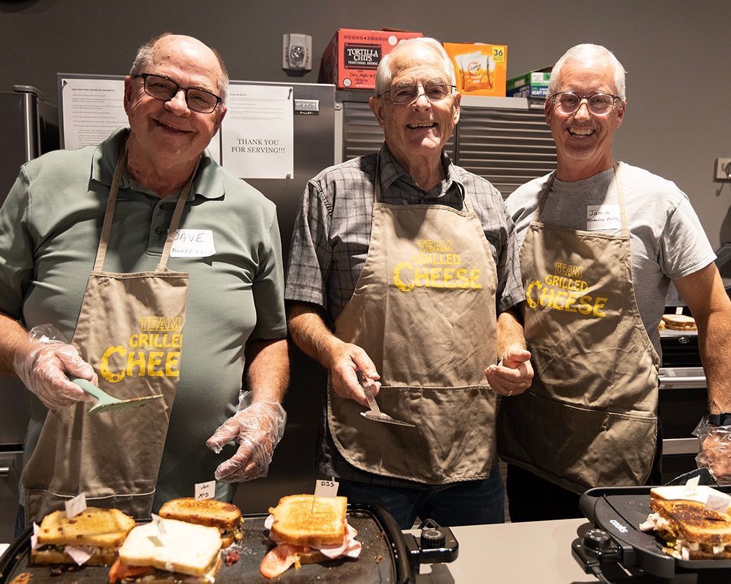 Three men are standing next to each other in a kitchen preparing food.