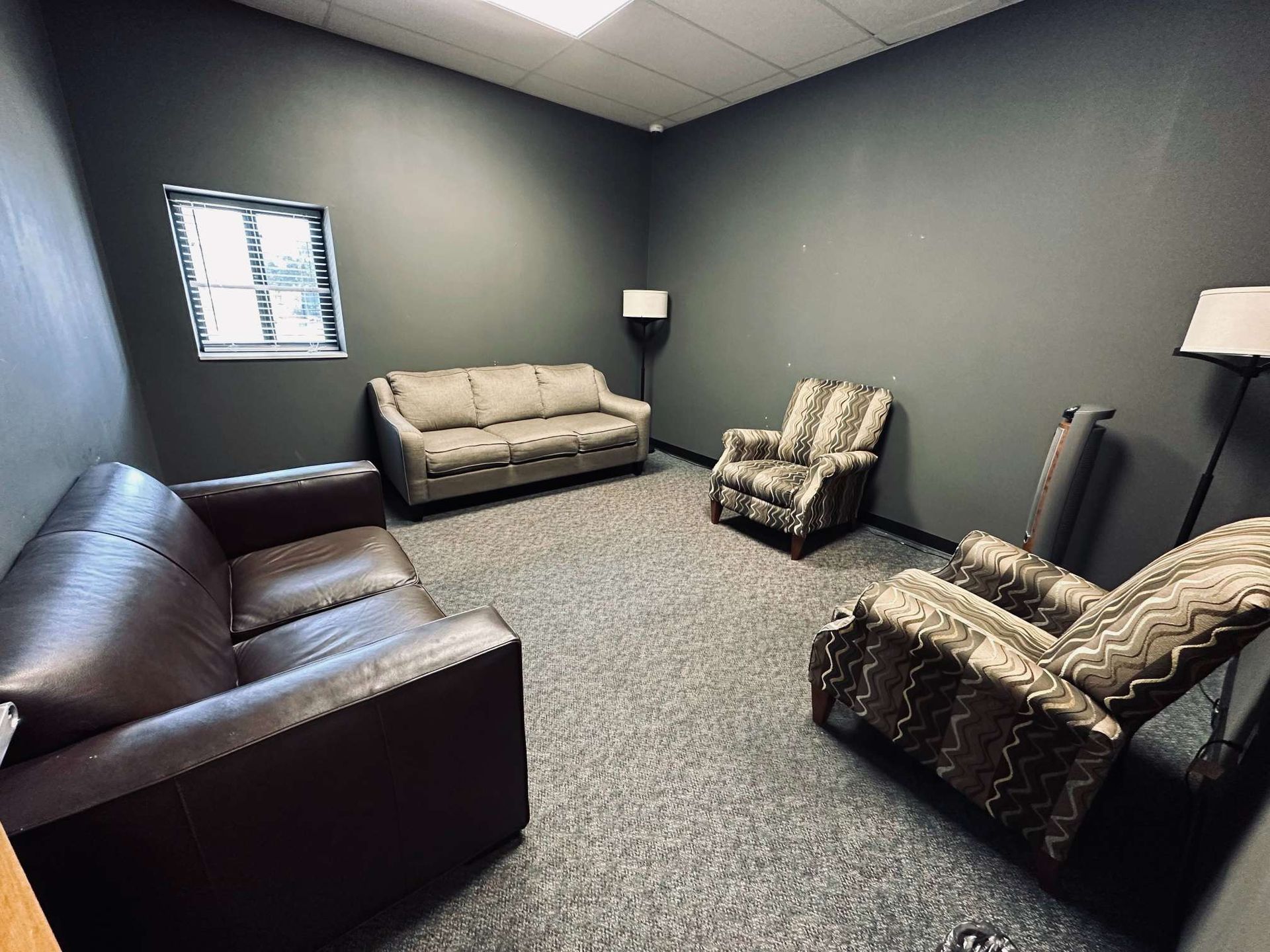 A living room with a couch , two chairs , and a lamp.