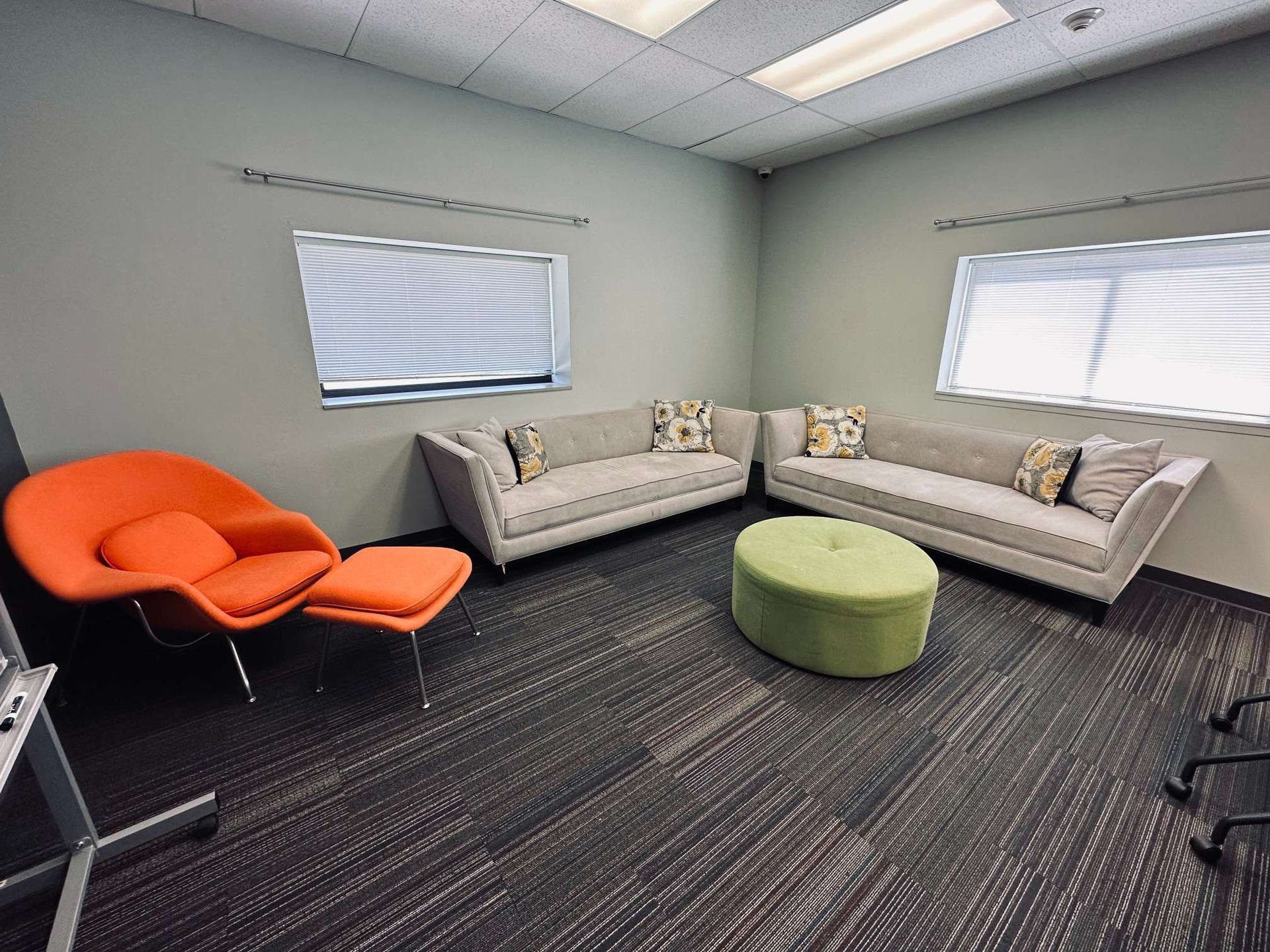 A living room with two couches , an orange chair , and an ottoman.
