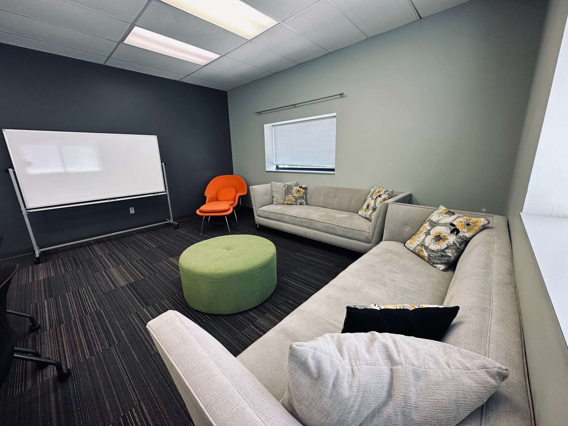 A living room with a couch , chair , ottoman and whiteboard.