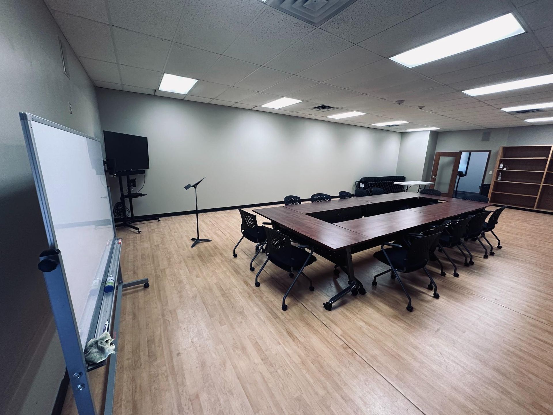 Conference room with large wooden table, chairs, whiteboard, and television.