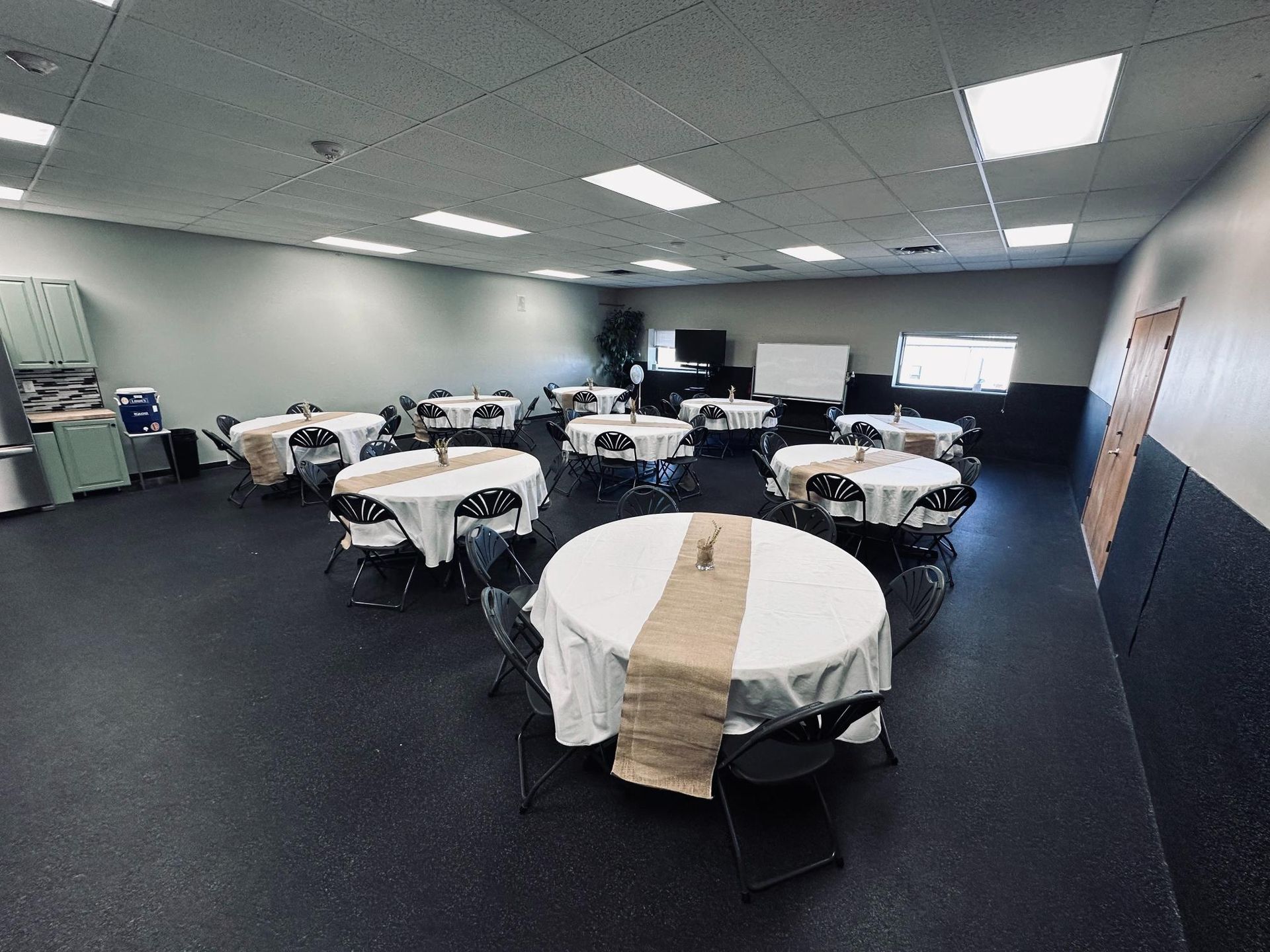 Event room with round tables, white tablecloths, burlap runners, and black chairs.