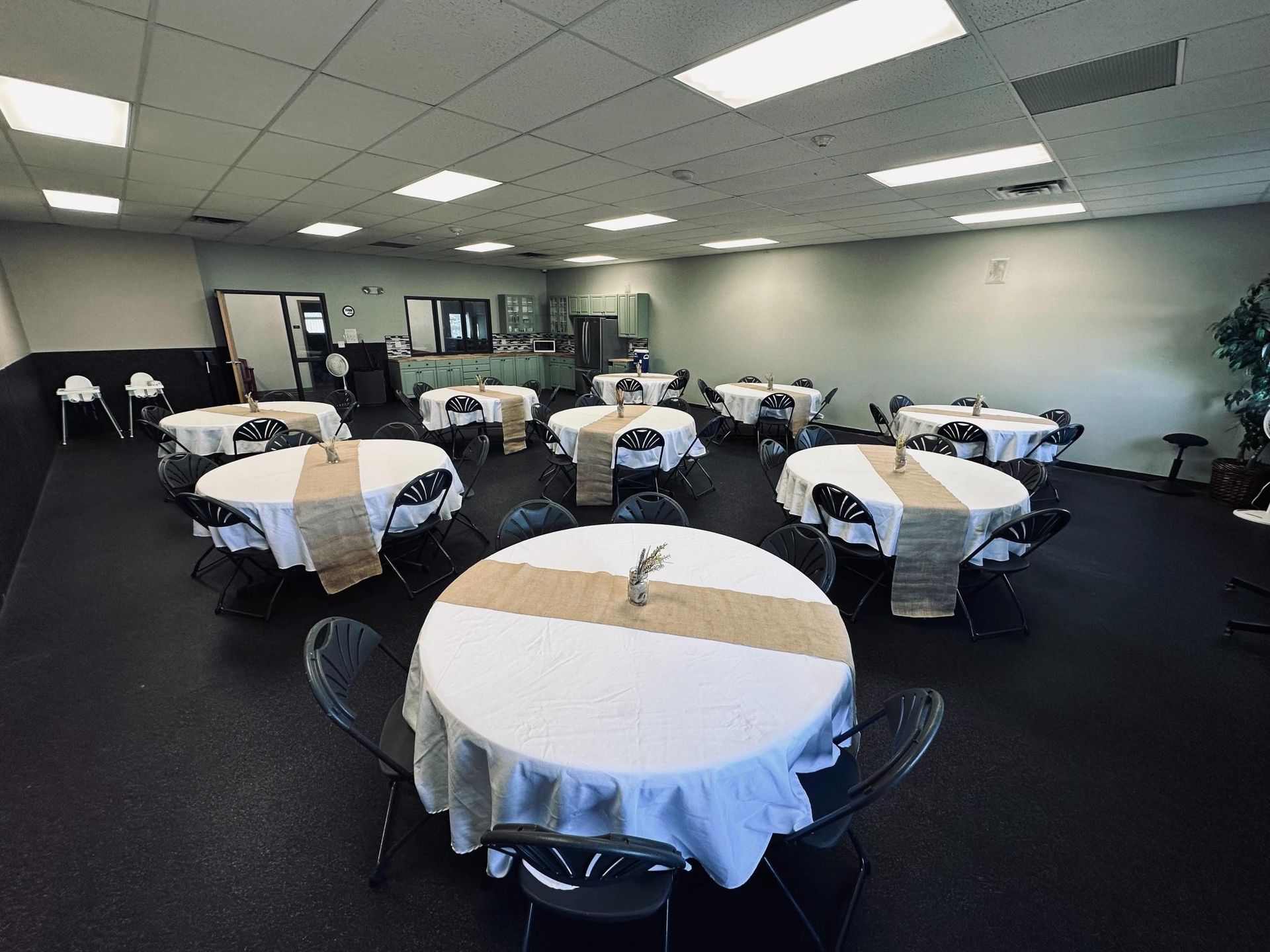 Empty event space with round tables, white tablecloths, burlap runners, and black chairs.
