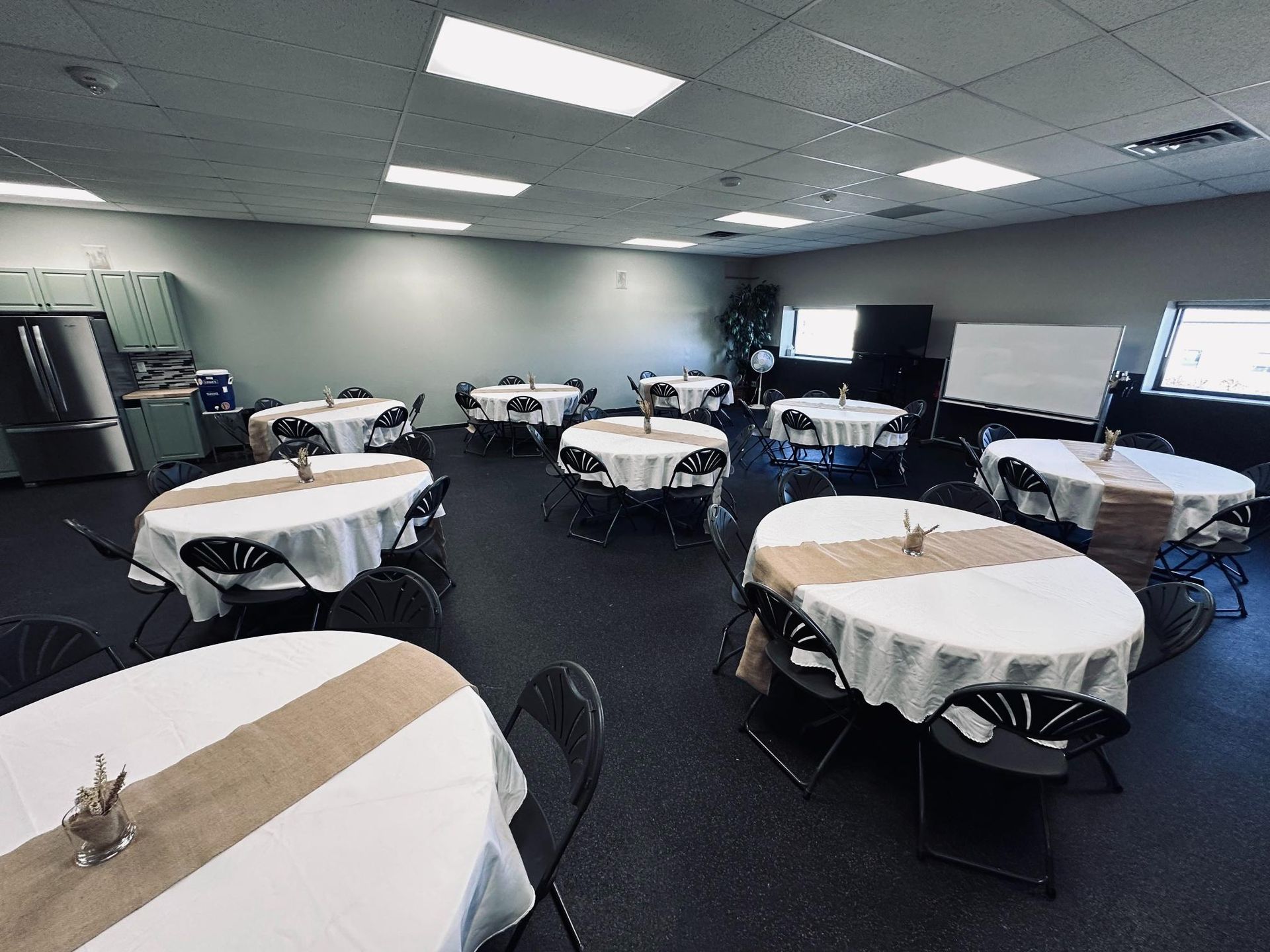 Event space with round tables, white tablecloths, burlap runners, and black chairs.