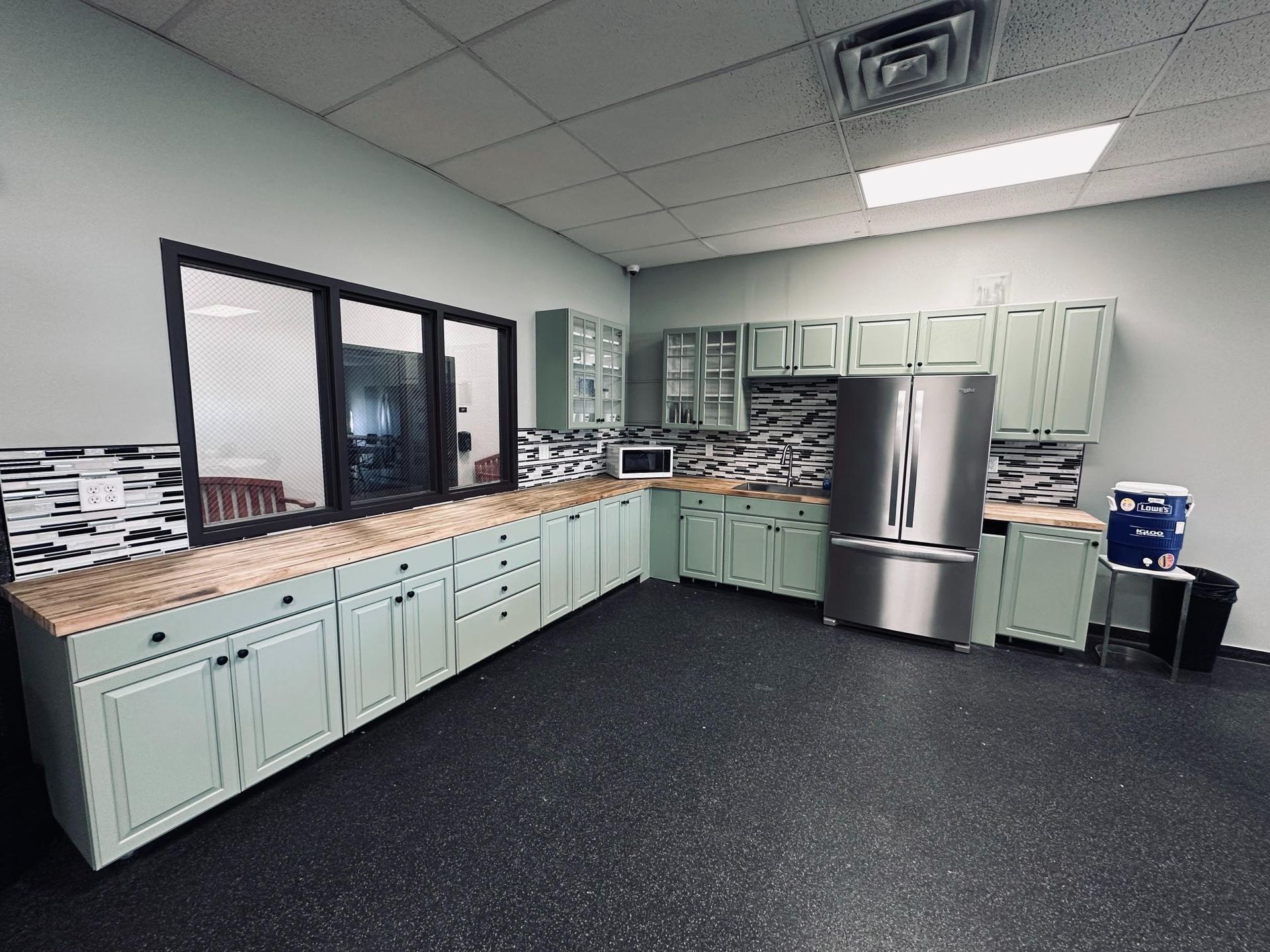 A kitchen with light green cabinets, stainless steel refrigerator, and a dark floor.