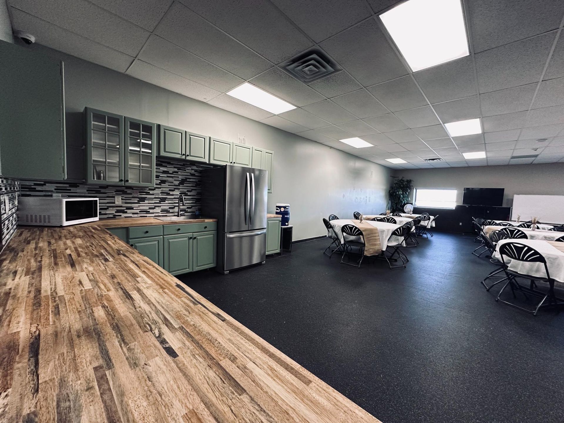 Kitchen area with counter, cabinets, refrigerator, and tables set for dining.