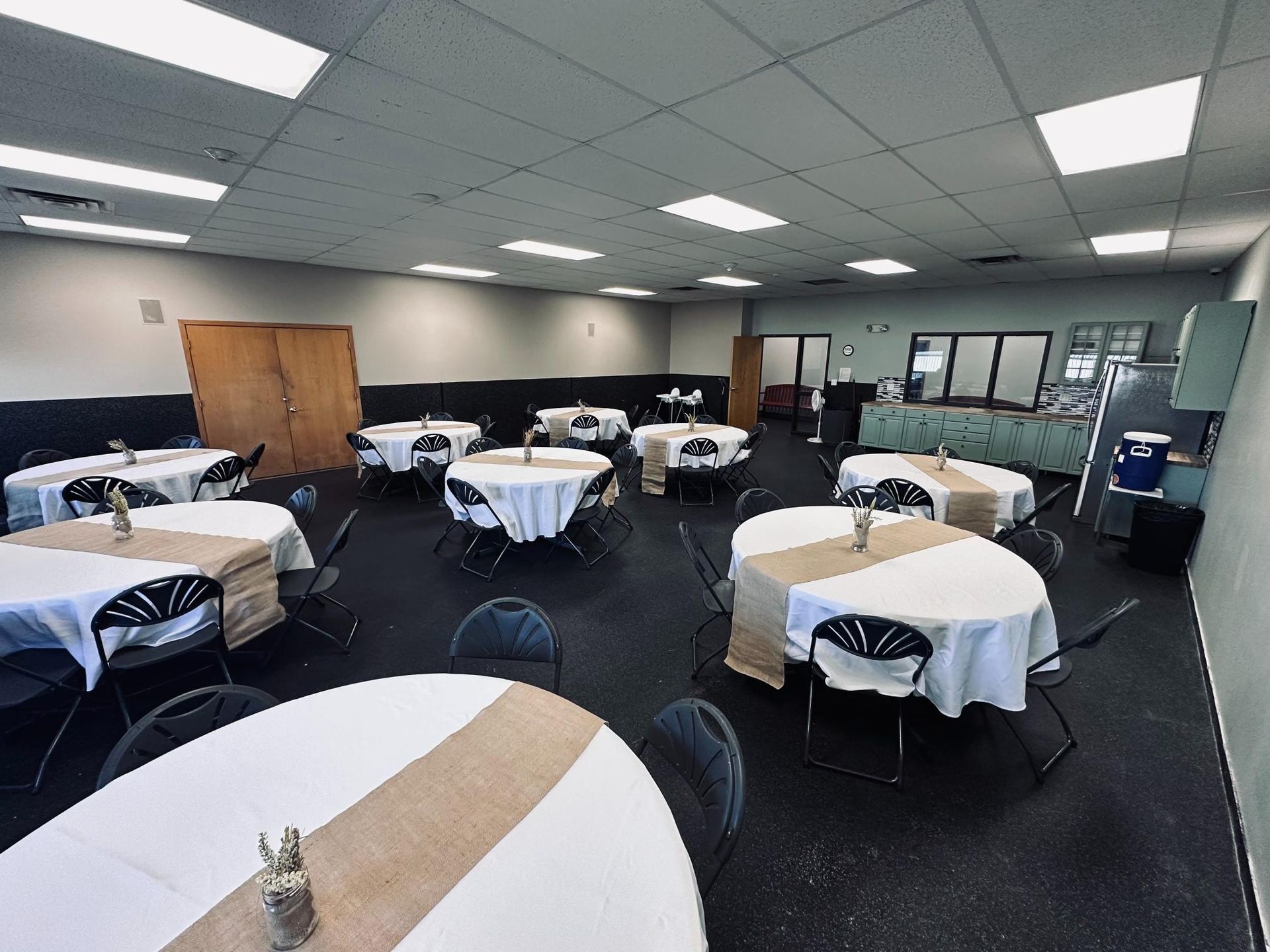 Event space with round tables covered in white linens and burlap runners; dark flooring.