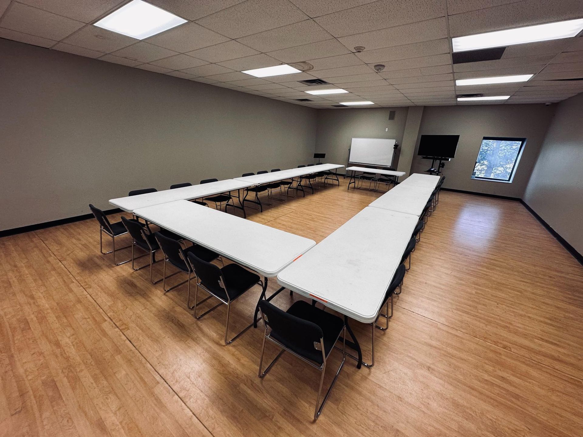 A U-shaped conference table with chairs in a room with wood flooring, and a window.