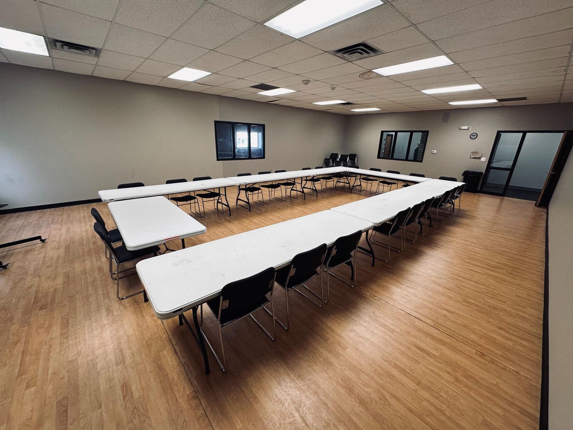 Empty conference room with U-shaped table and black chairs, wood floor, gray walls.