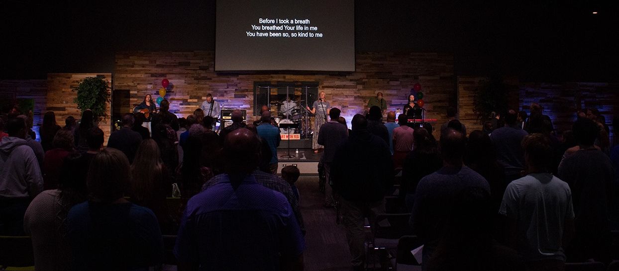 A band performs on stage in front of a crowd. Lyrics are projected on a screen.