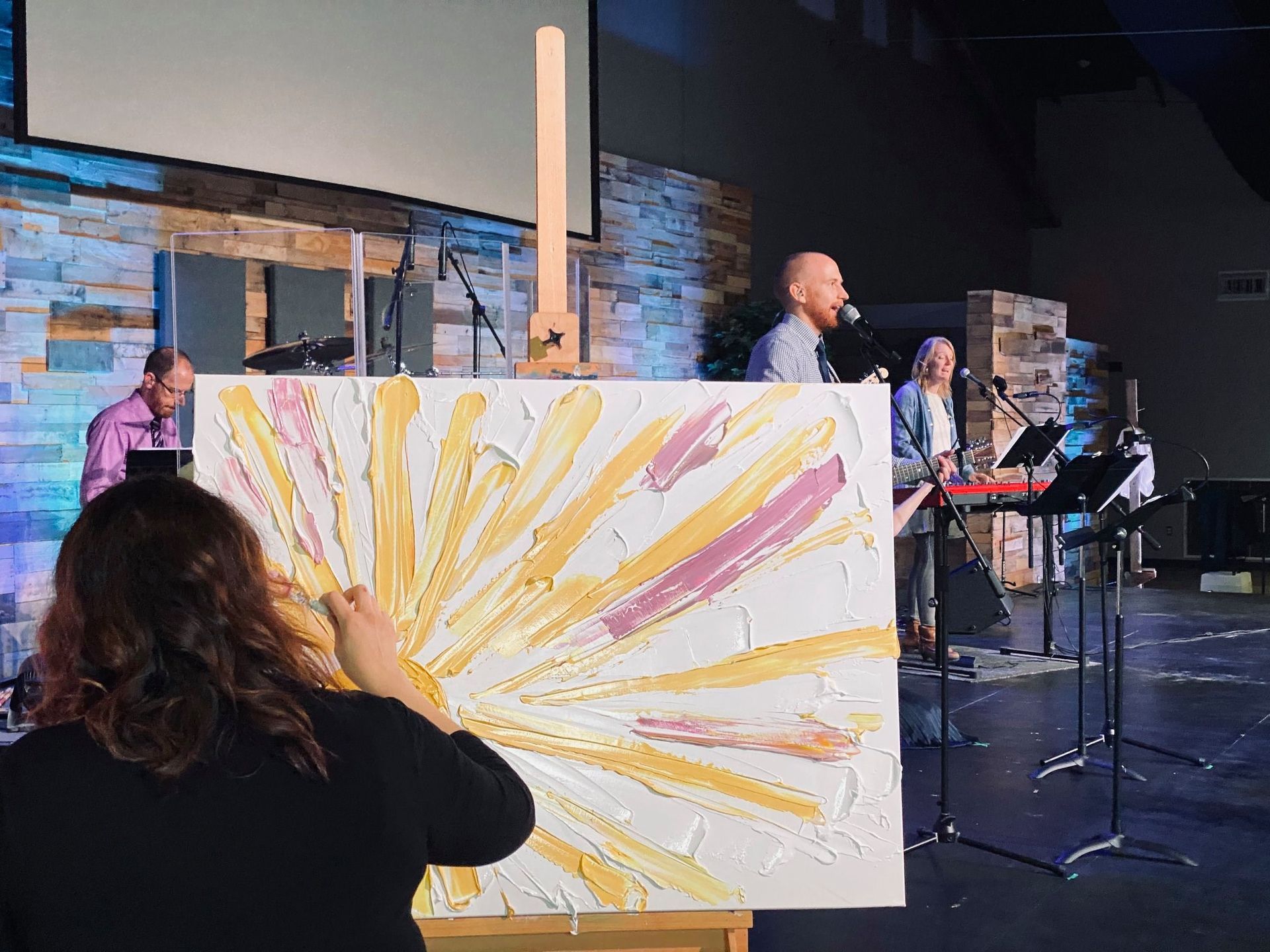 A woman is holding a large painting in front of a group of people on a stage.