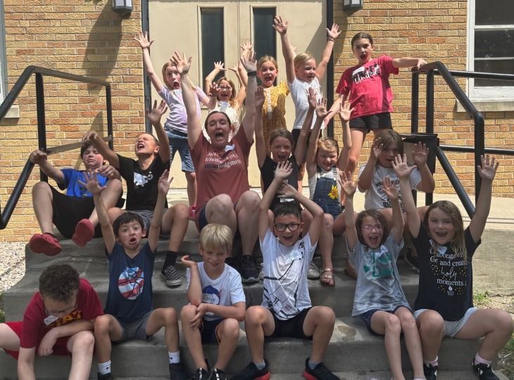 Group of children on stairs with arms raised in front of a building. Sunny day.