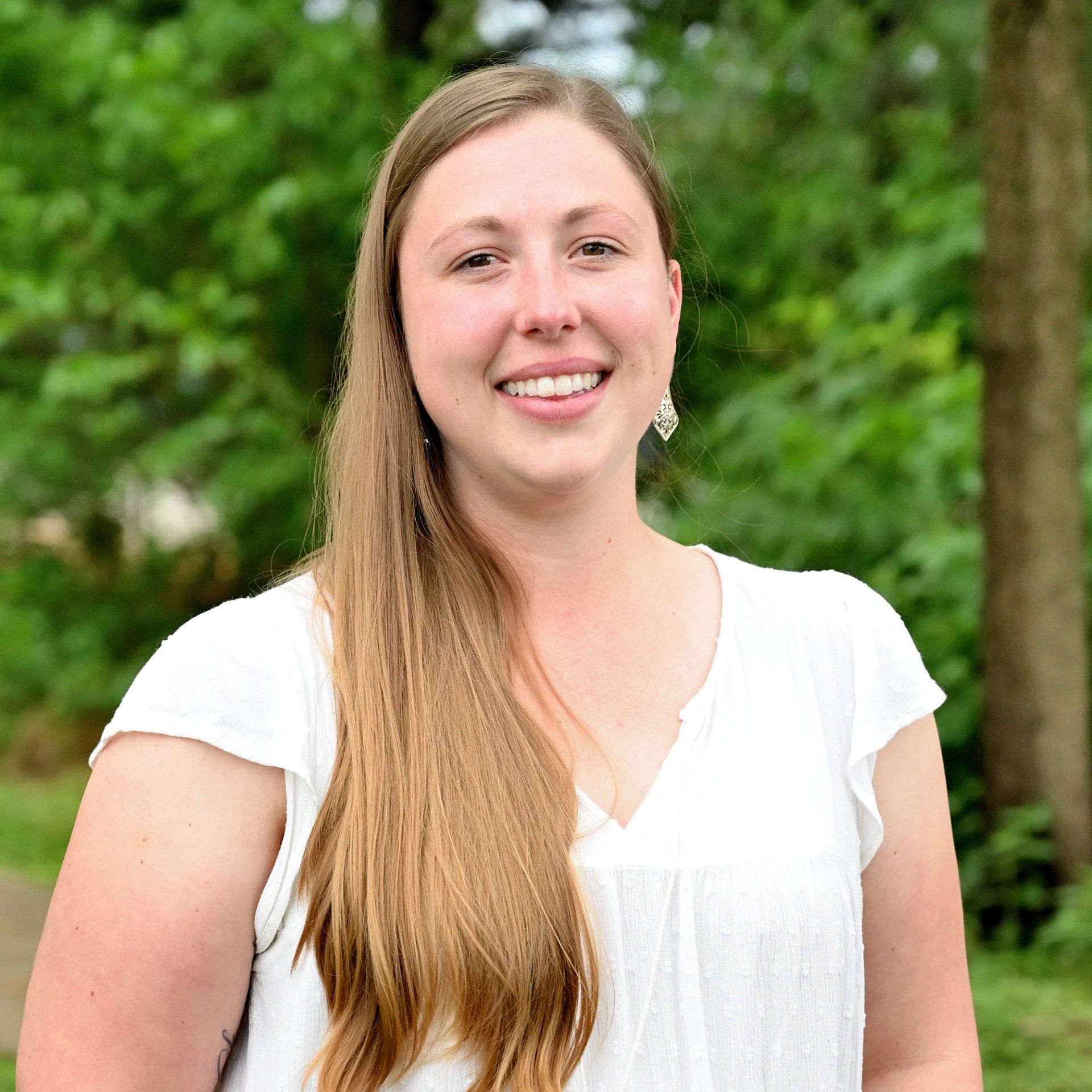 A woman with long hair is wearing a white shirt and smiling for the camera.