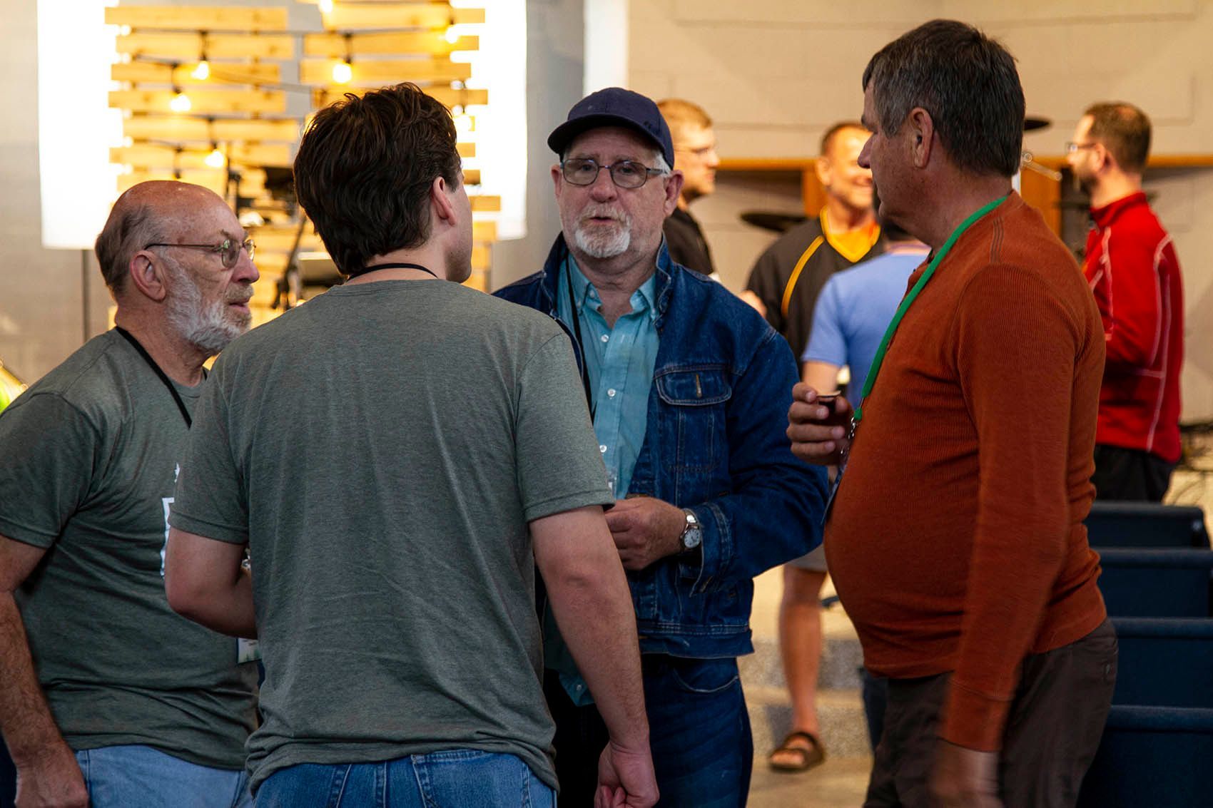 A group of men are standing in a room talking to each other.