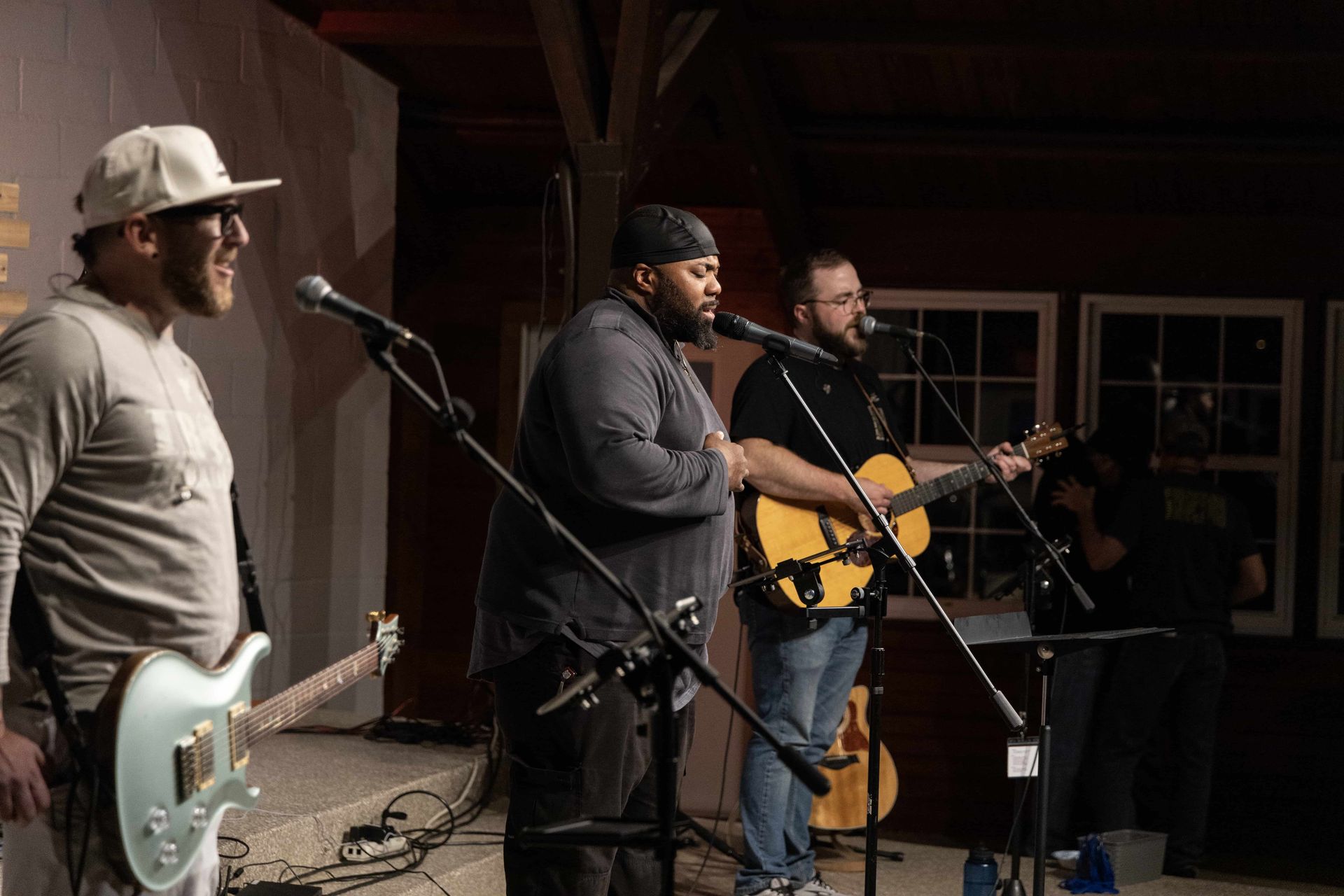 Three men are playing guitars and singing into microphones on a stage.