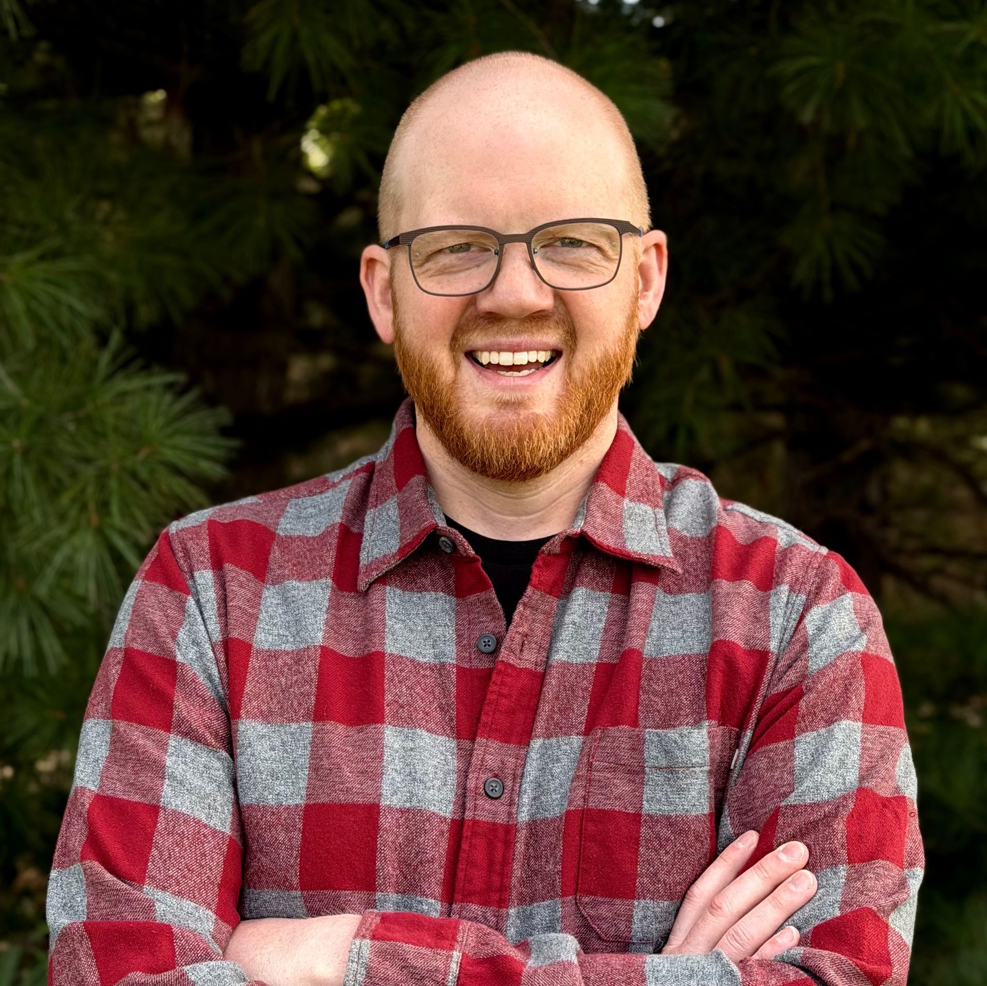 A man with a beard and glasses is smiling with his arms crossed.