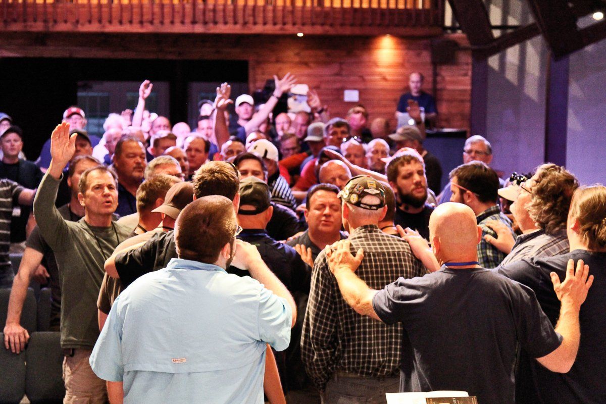 A large group of people are standing in a room with their hands in the air