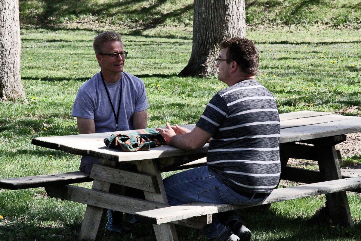 Two men are sitting at a picnic table talking to each other.
