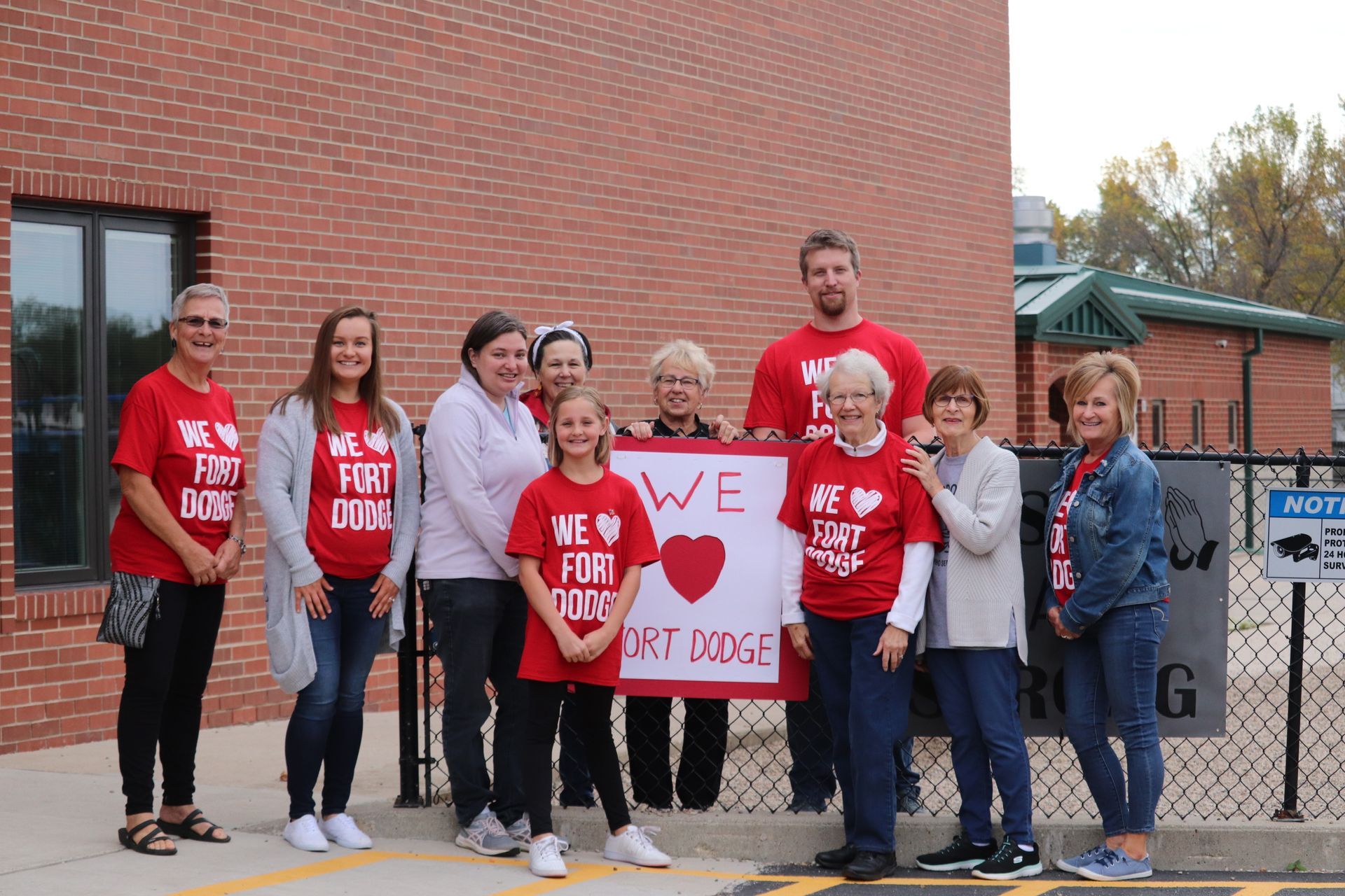 A group of people standing in front of a brick building holding a sign that says `` we love fort ridge ''.