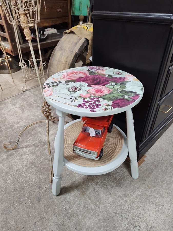 Small painted table with floral top, red toy truck on lower shelf.