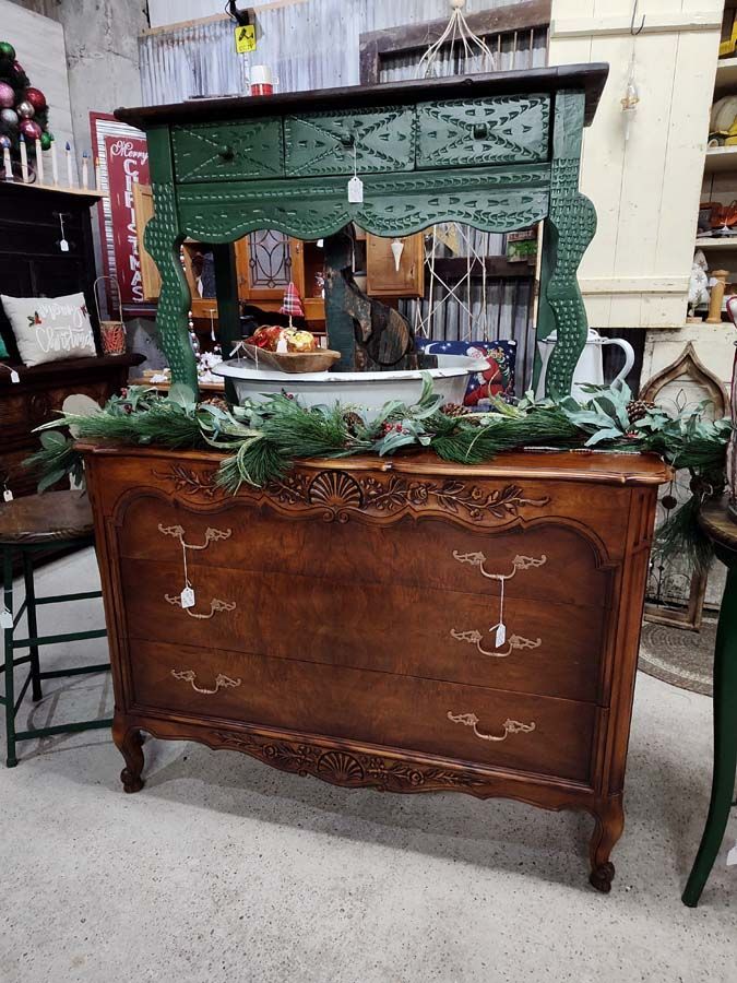 A vintage wooden dresser with a green-painted top and a garland, in a shop setting.