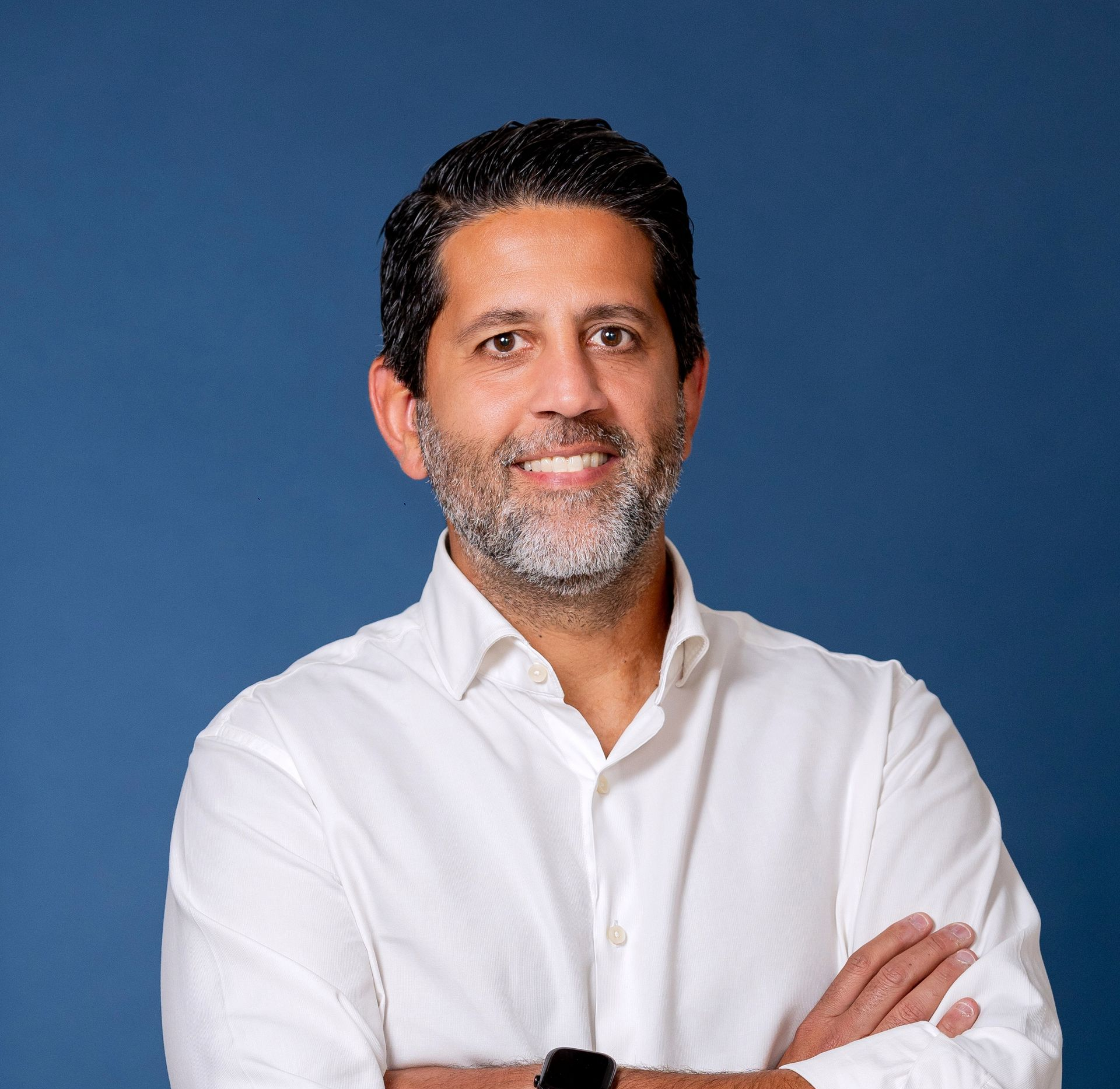 Smiling Josean Arroyo Pont in a navy blazer and white shirt against a dark blue studio background