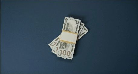 A stack of U.S. hundred-dollar bills on a blue surface