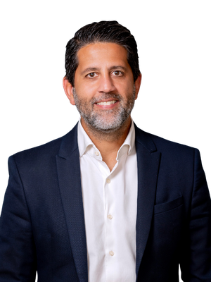 Josean in a blazer and open-collared shirt, smiling with a pocket square, studio shot.