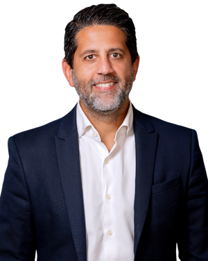 Smiling Josean Arroyo Pont in a navy blazer and white shirt against a dark blue studio background.