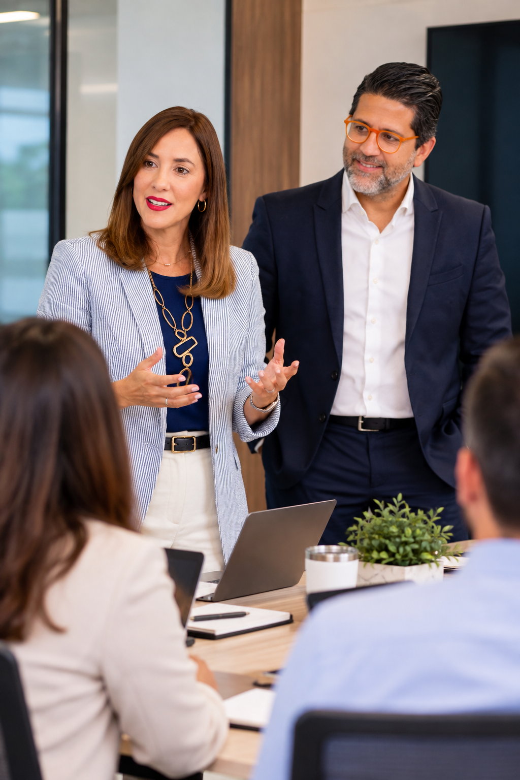 Two coworkers in a meeting, smiling across a conference table with a laptop and notebook.