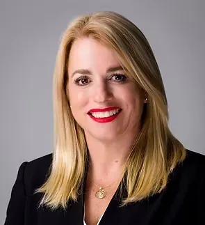 Portrait of a smiling blonde woman in a black blazer against a gray background