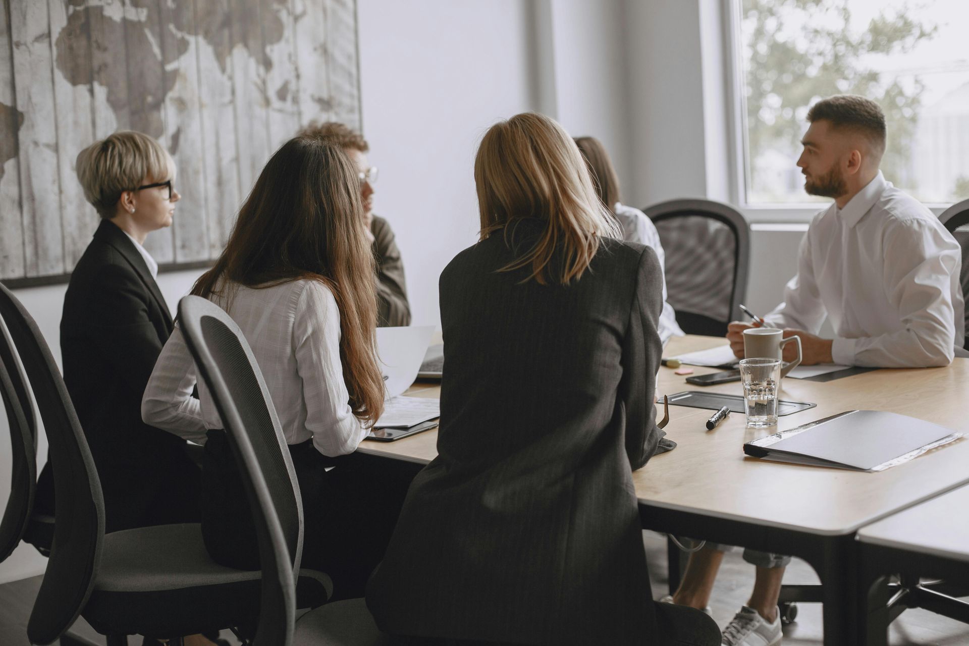 Small group meeting around a table in a bright office, discussing over coffee and papers.