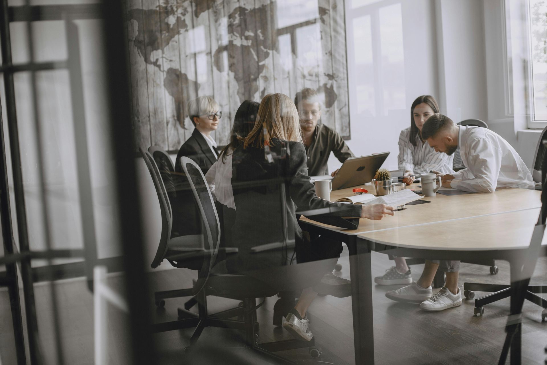 People in a conference room, listening to a presentation at a whiteboard. Natural light from a large window.