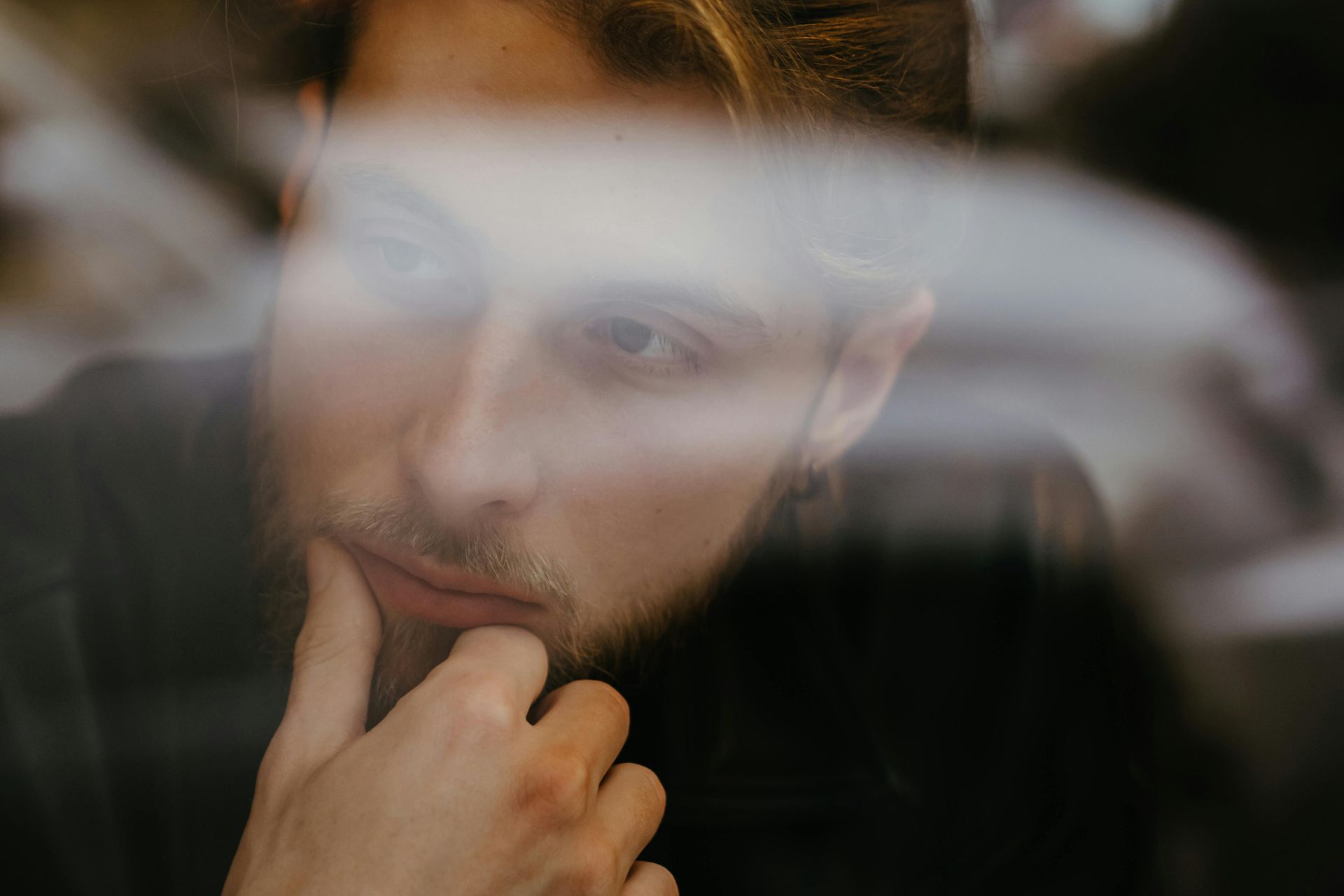 Close-up of a person with hand on chin, seen through a blurred reflective surface.